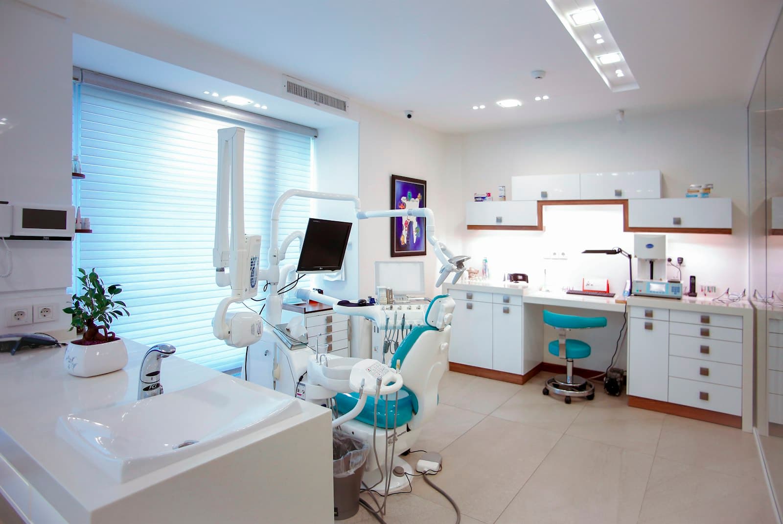 A bright, modern dental treatment room with a dental chair, cabinetry and a large window