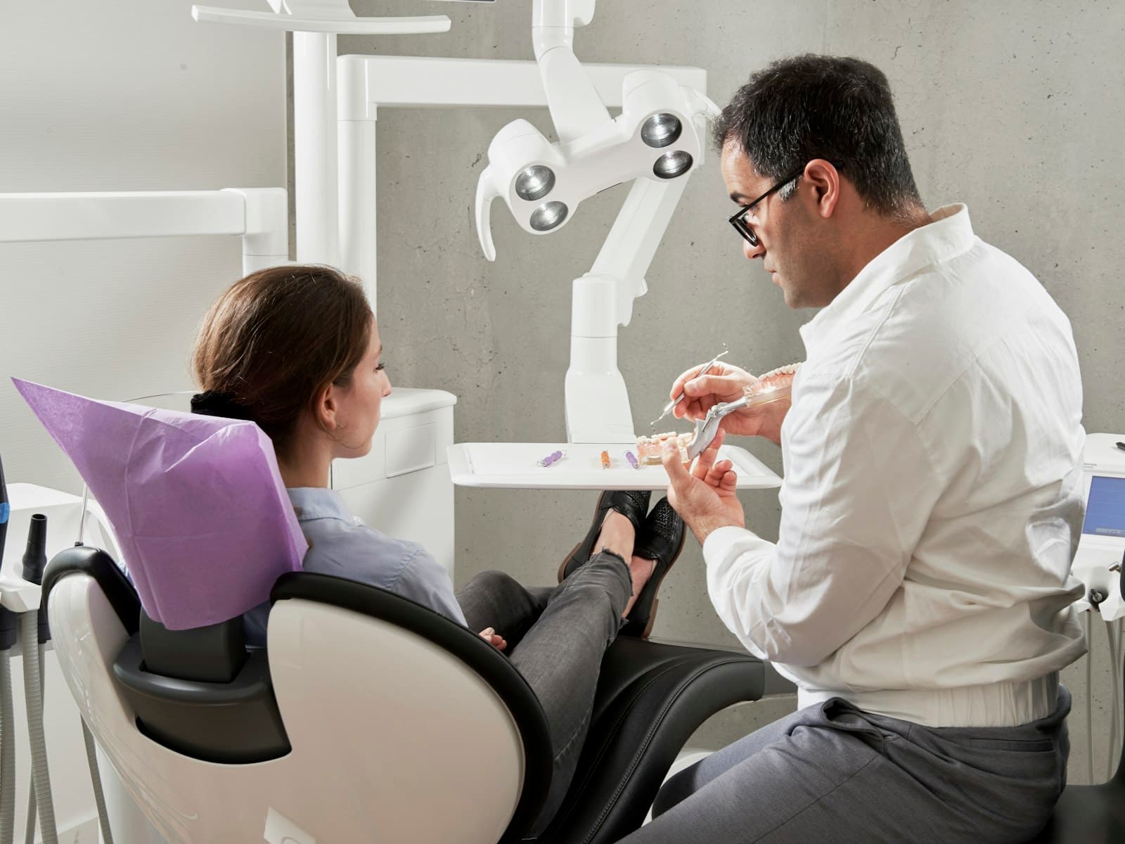 A dentist in a white shirt sitting beside a patient in a dental chair, discussing her treatment